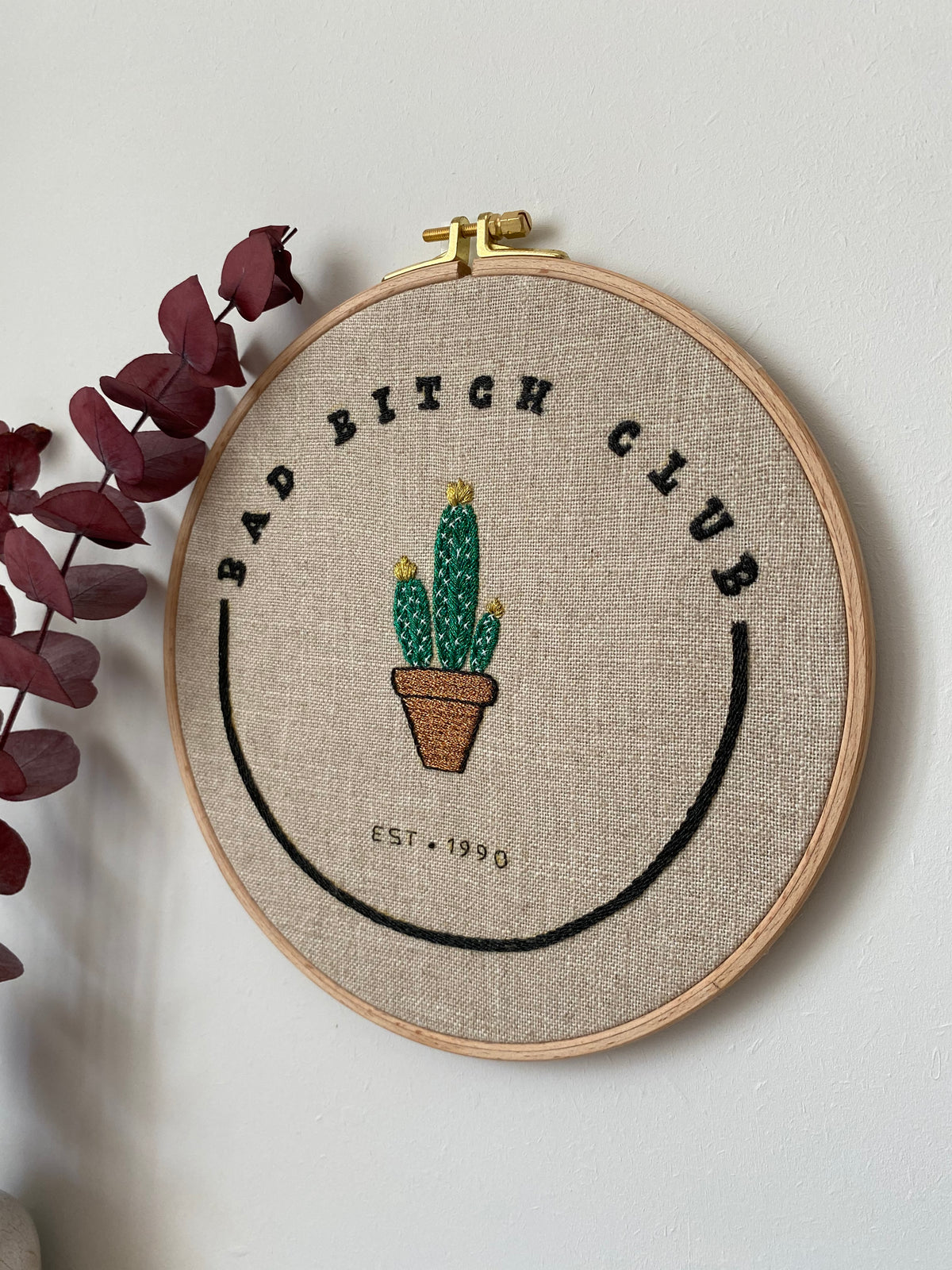 The Bad Bitch Club cactus hoop on a white wall beside dried eucalyptus