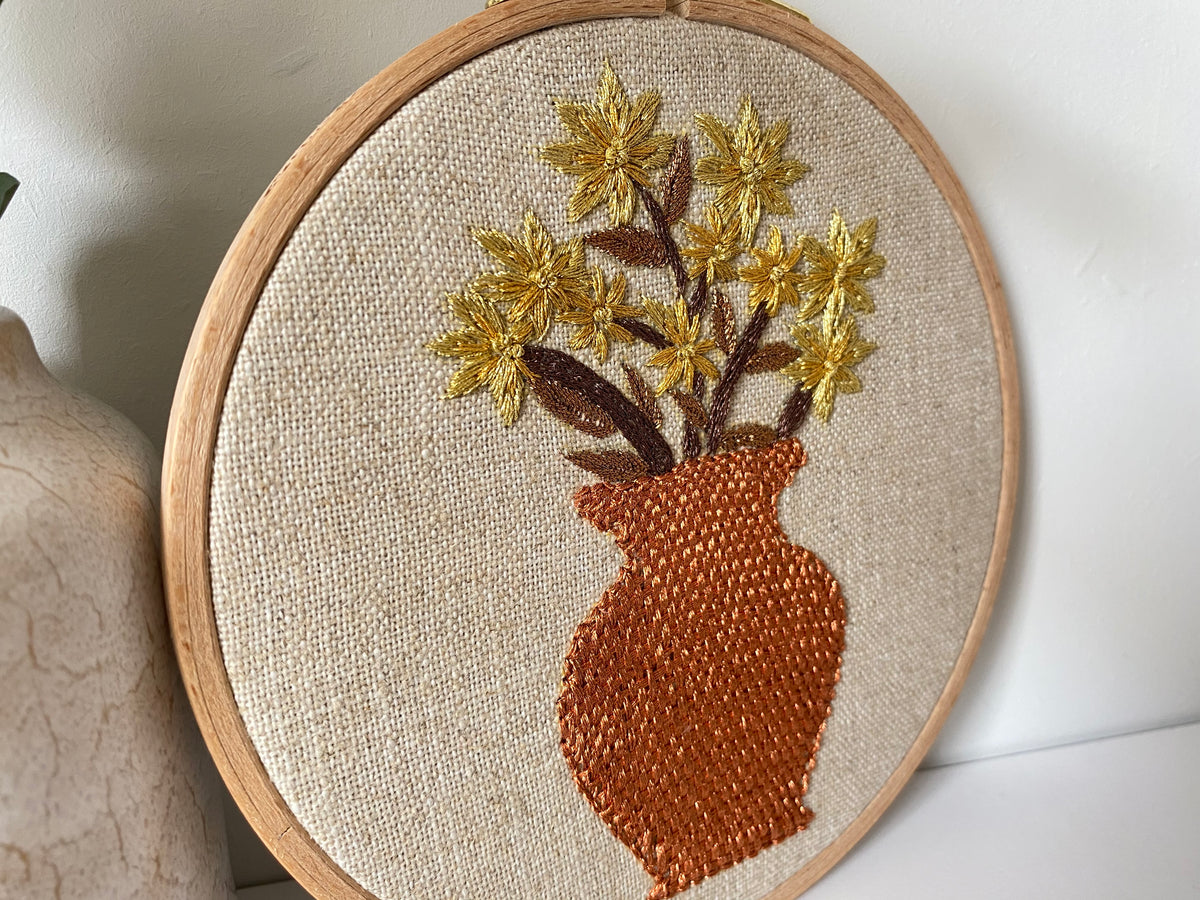 Close view of the terracotta vase design, the vase worked in dense rust thread with golden blooms above