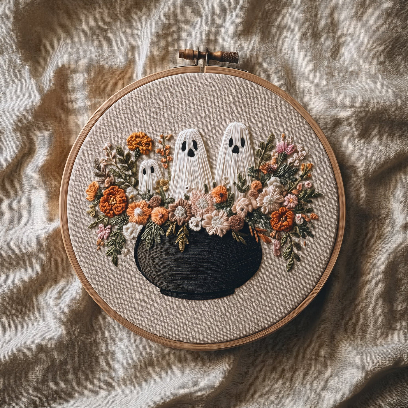 Three ghosts rising from a black cauldron of autumn flowers, finished hand embroidery hoop photographed in full