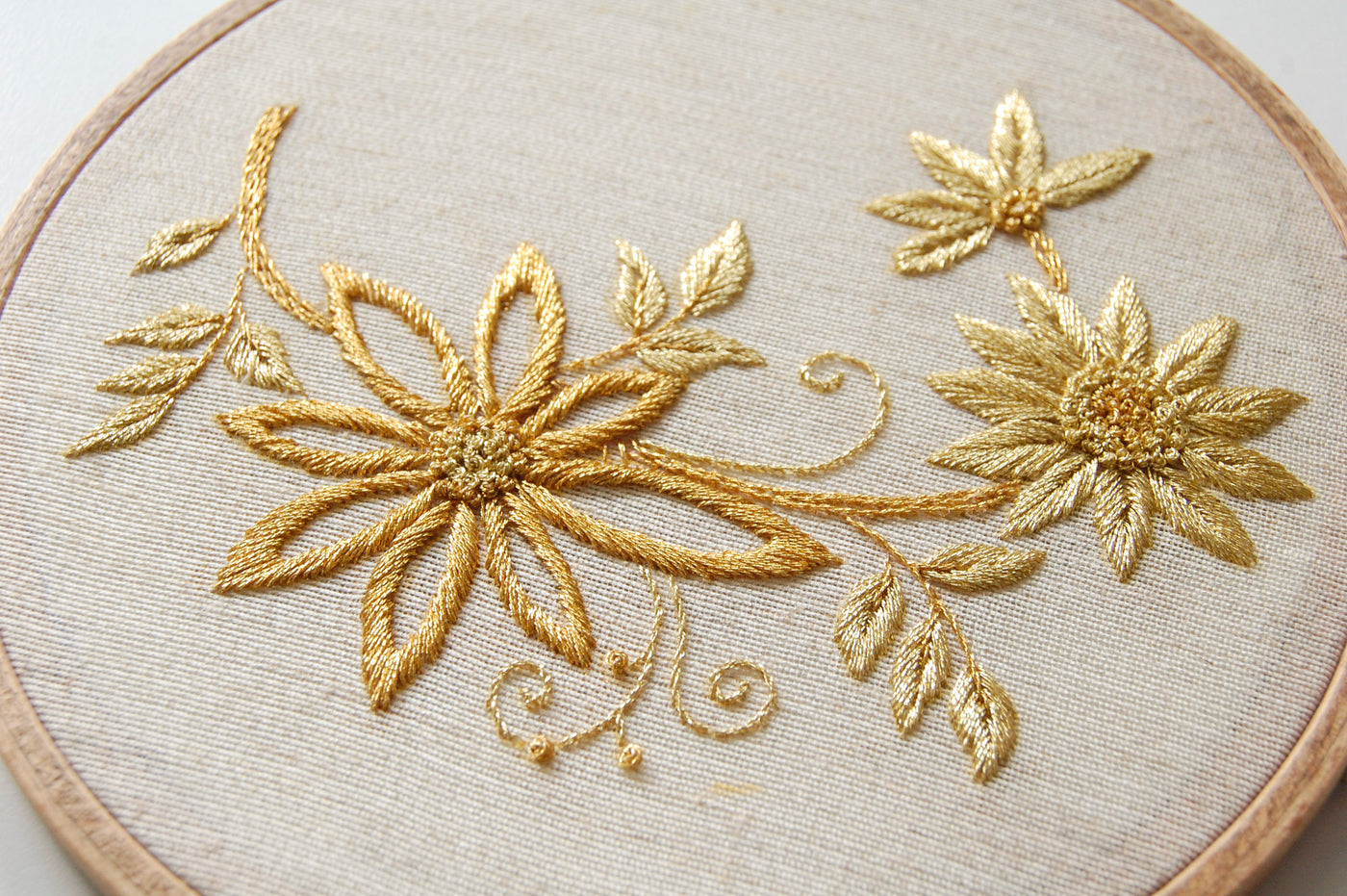 Close view of the gilded daisy spray showing the raised metallic stitching on linen