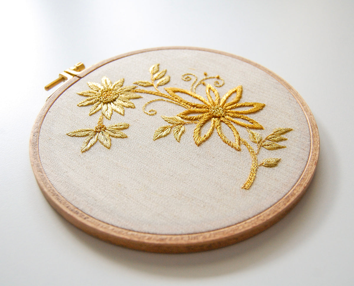 The gilded daisy spray hoop seen at an angle, with light catching the gold thread