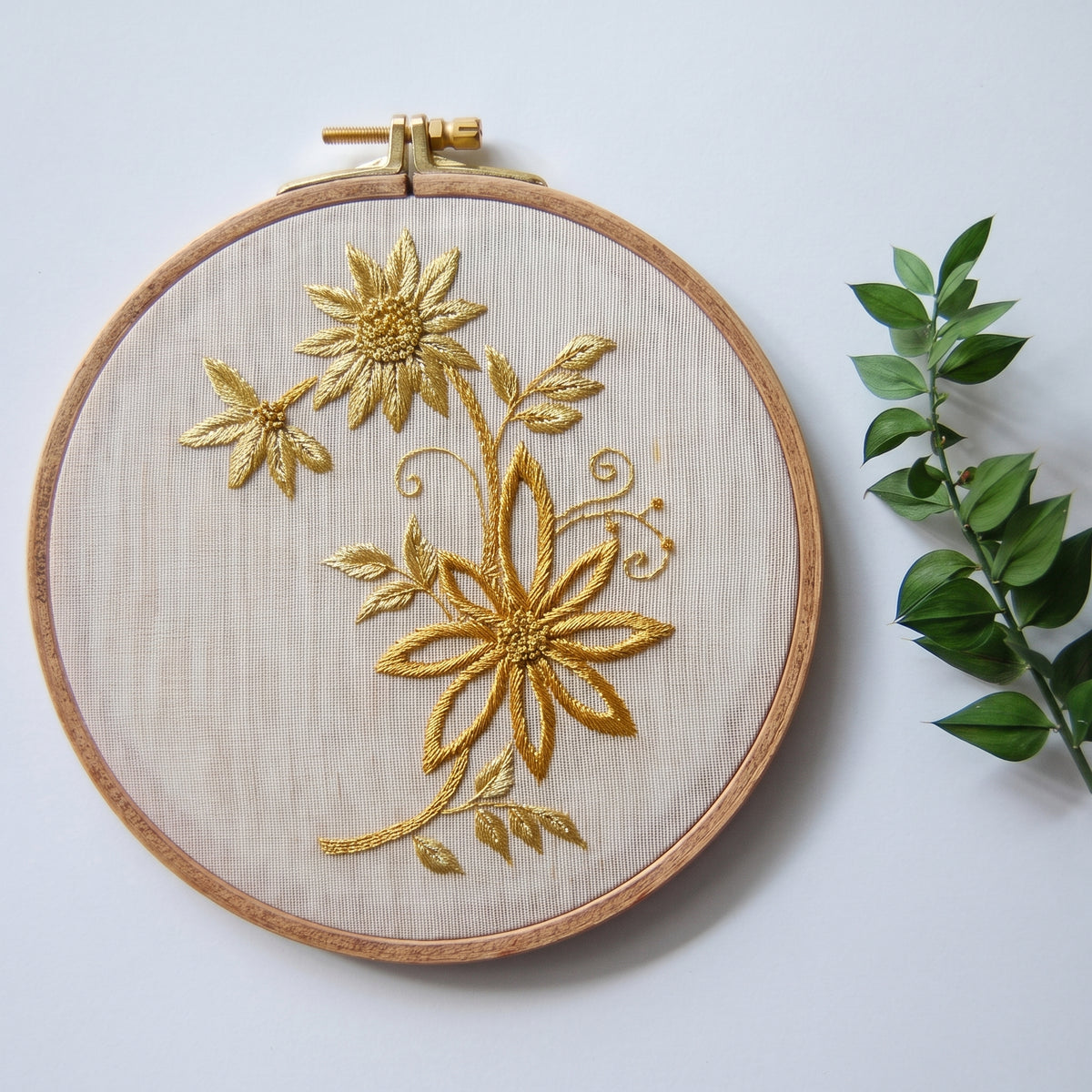 The gilded daisy spray hoop beside a sprig of green foliage