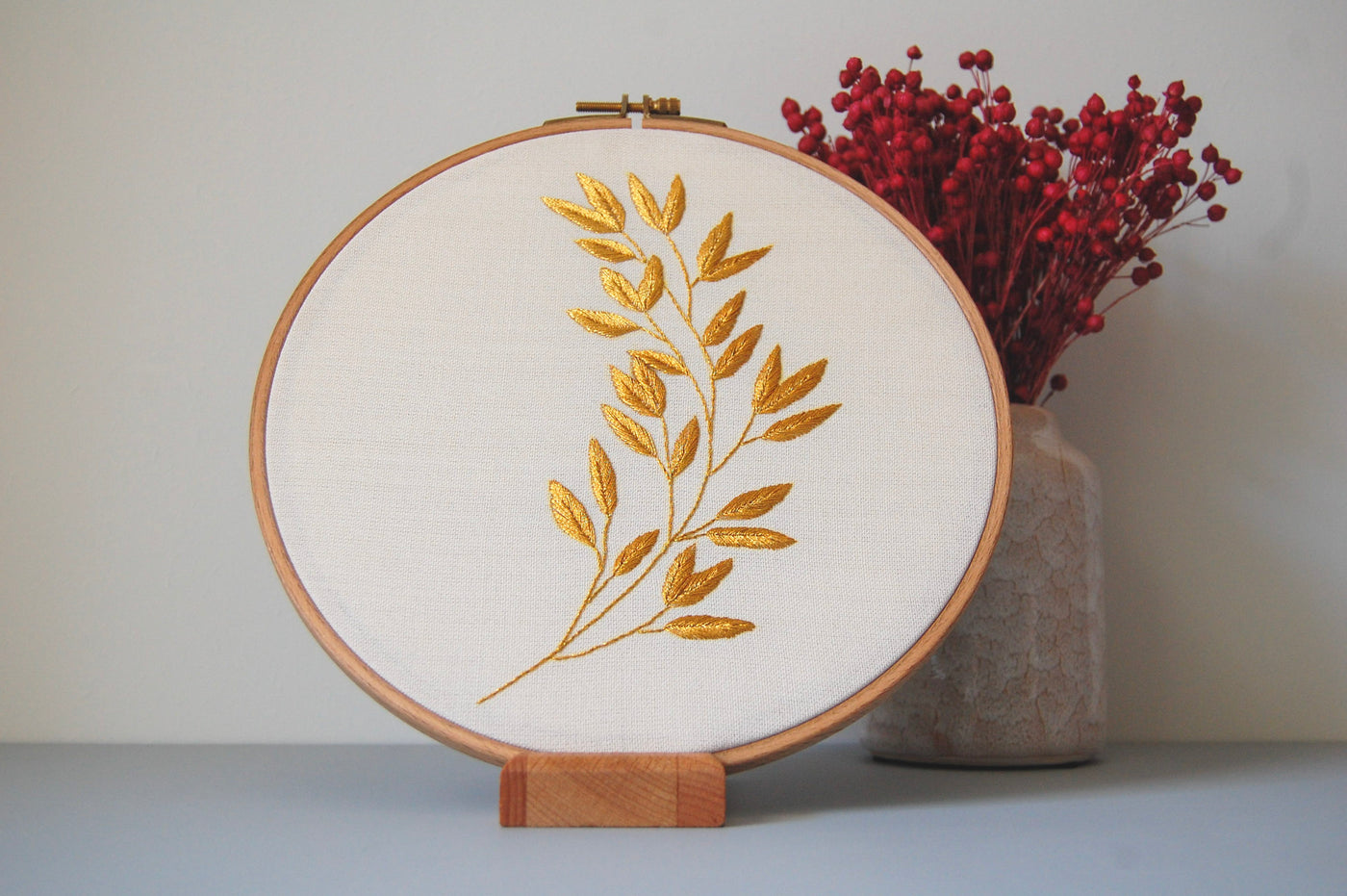 The golden laurel sprig hoop beside dried pink flowers in a stone vase