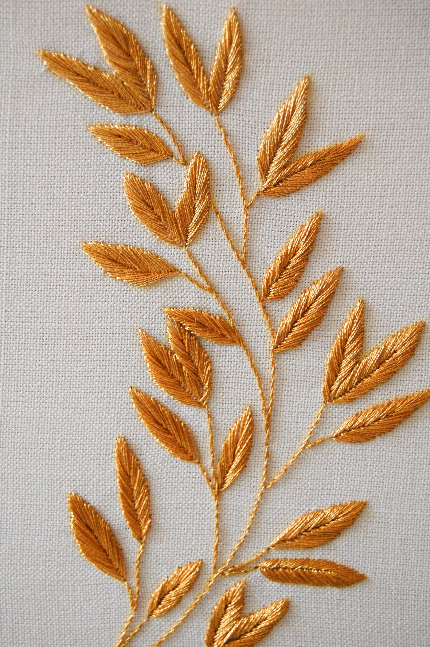 Close view of the golden laurel sprig, each leaf worked in gold thread on linen