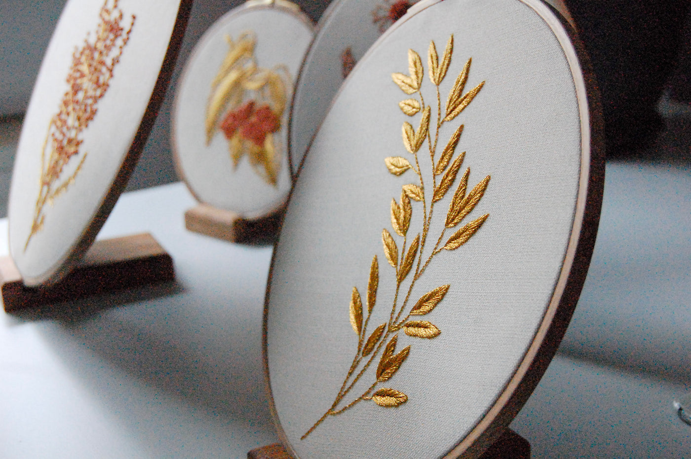 The golden laurel sprig hoop among other embroidered hoops on wooden stands