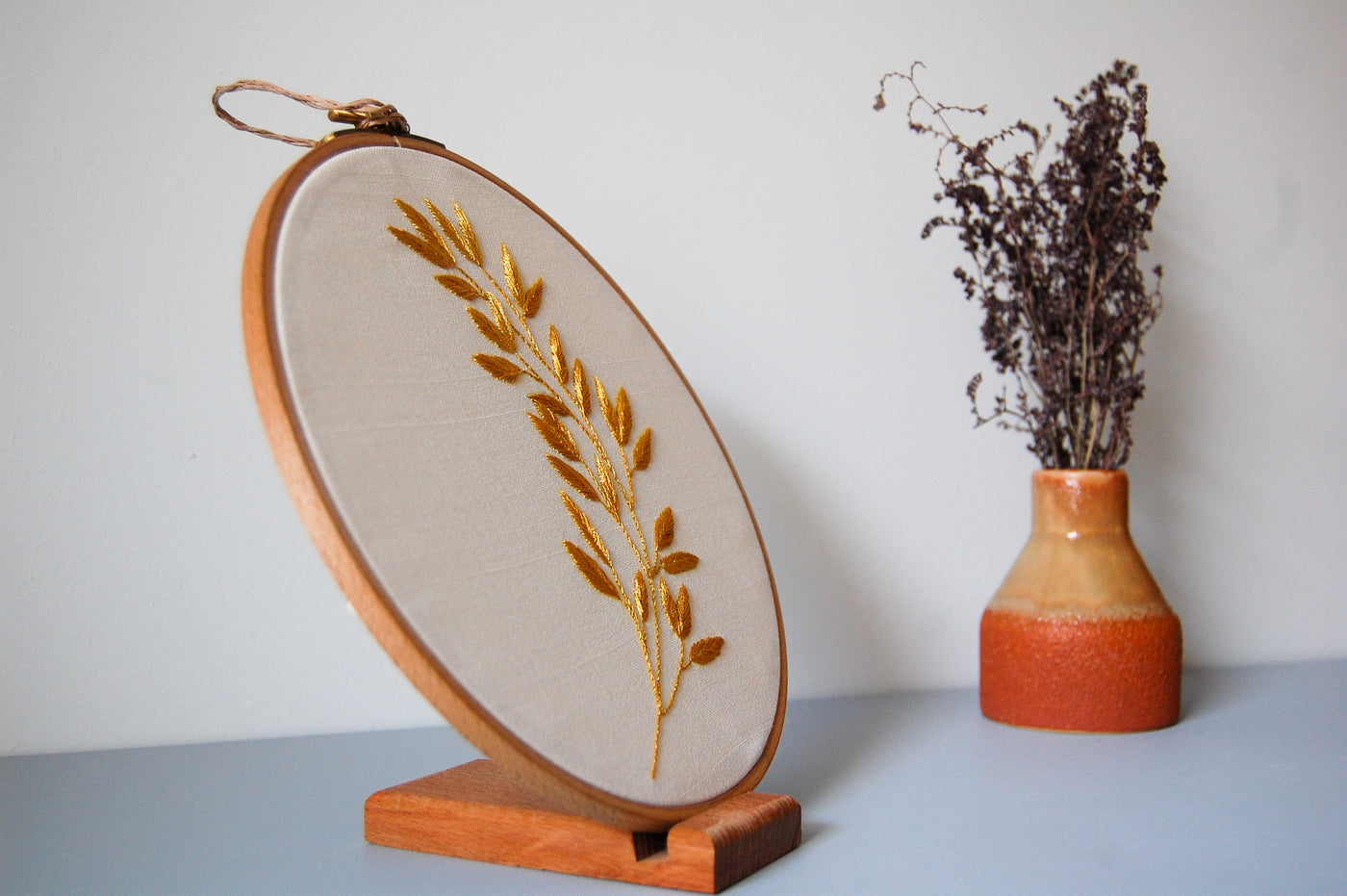 The golden laurel sprig hoop on its stand beside a terracotta vase of dried flowers