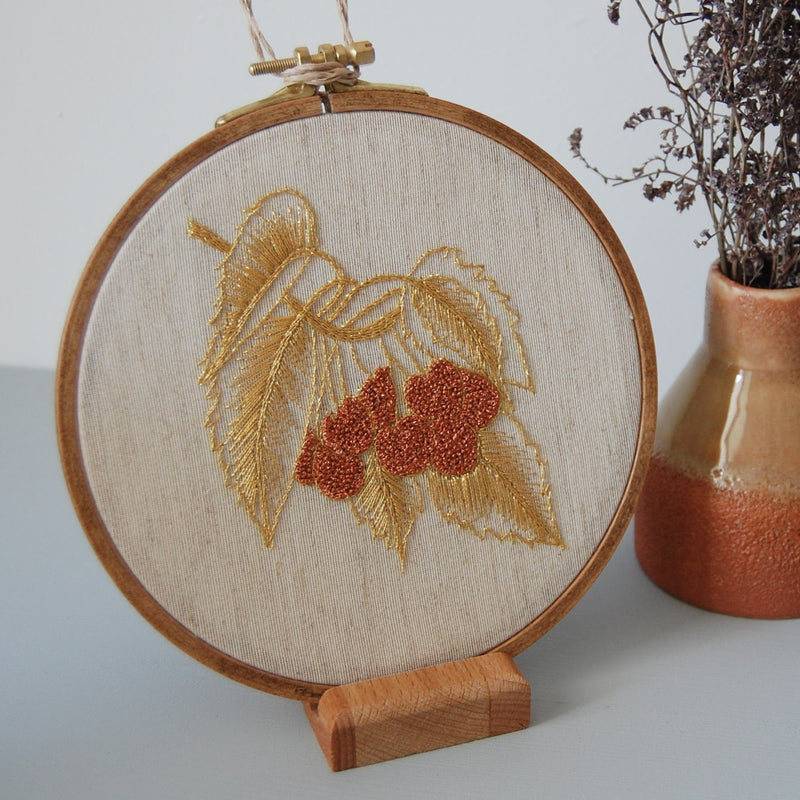 Golden leaves and a cluster of red berries embroidered in a wooden hoop on a display stand