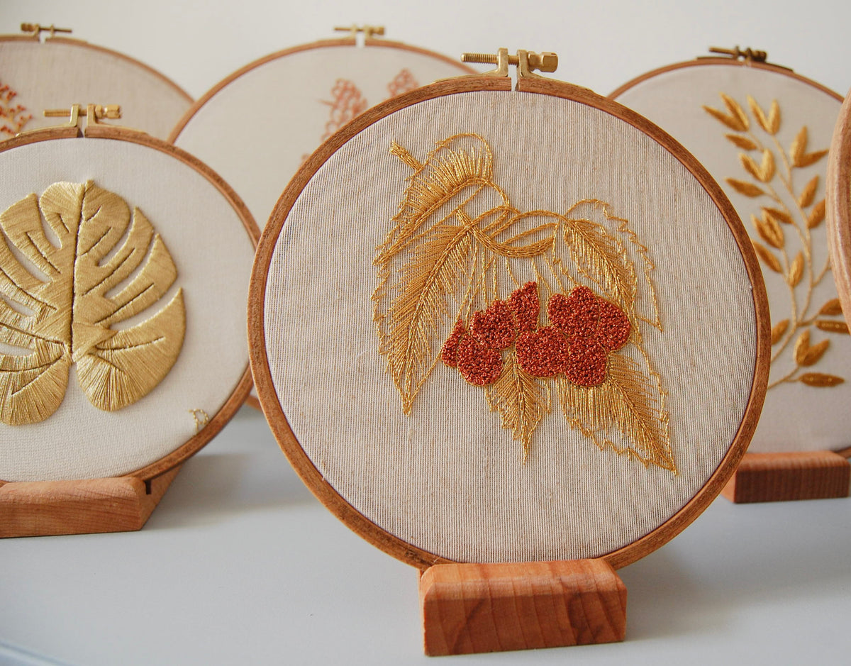The golden leaves and red berries hoop among other embroidered hoops on wooden stands