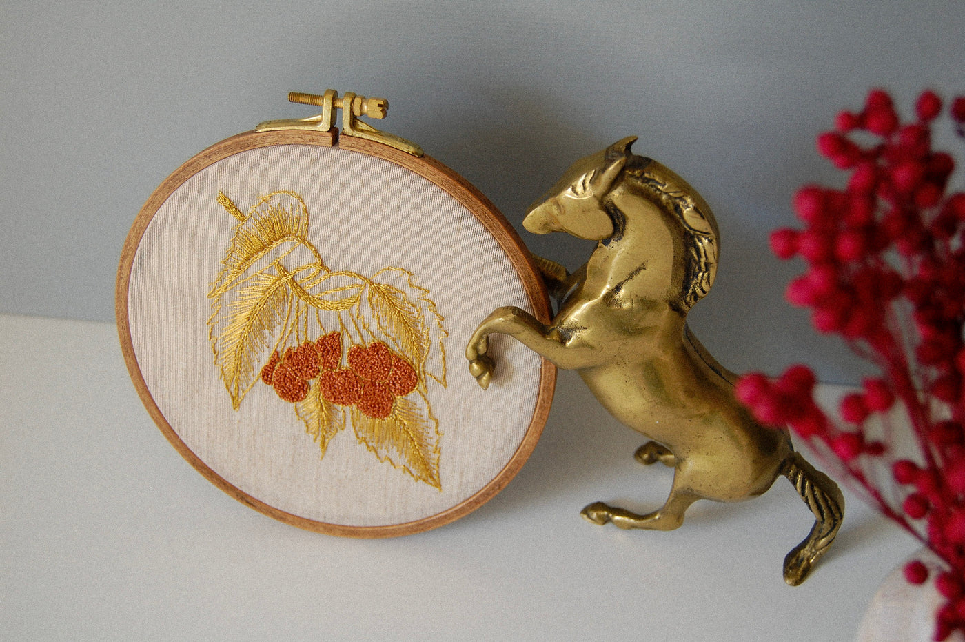 The golden leaves and red berries hoop beside a brass horse figure and red berries