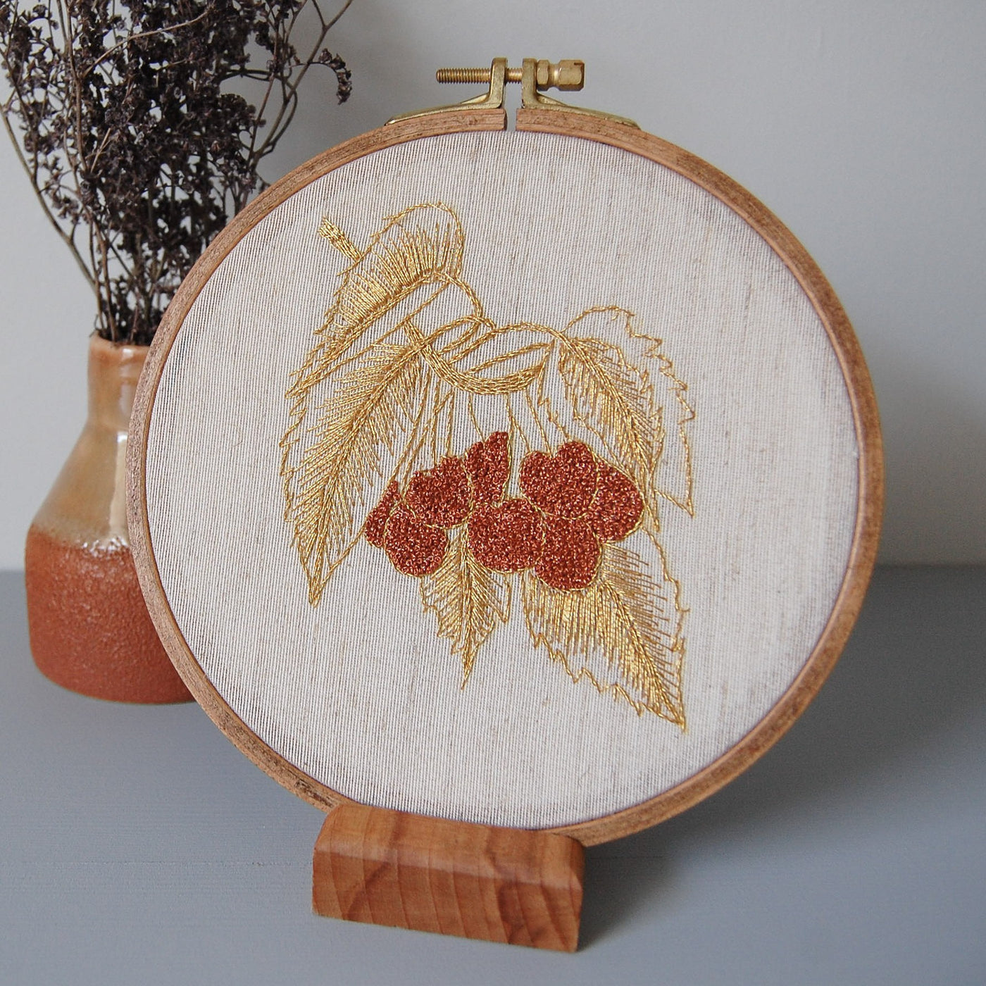 Close view of the golden leaves and red berries design beside a vase of dried flowers