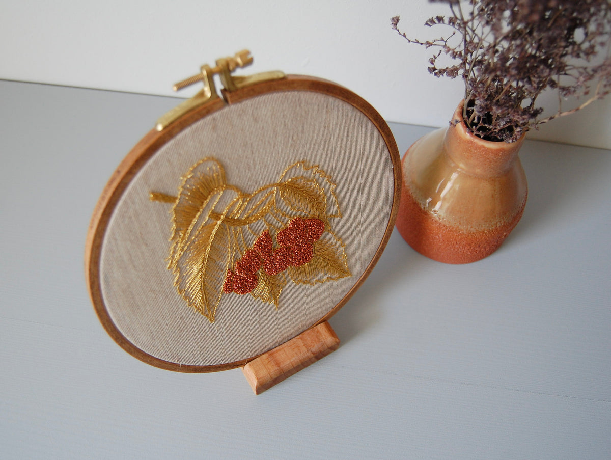 The golden leaves and red berries hoop on its stand beside a terracotta vase of dried flowers
