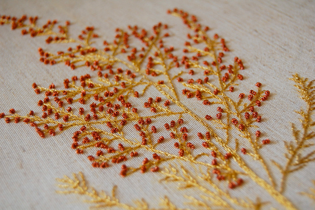 Close view of the wildflower spray, with tiny red-orange berry stitches worked over gold stems