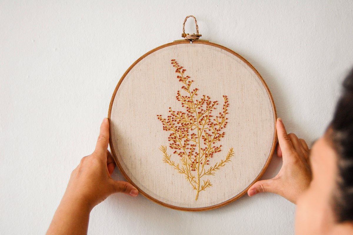 Hands hanging a botanical hand embroidery hoop on a white wall