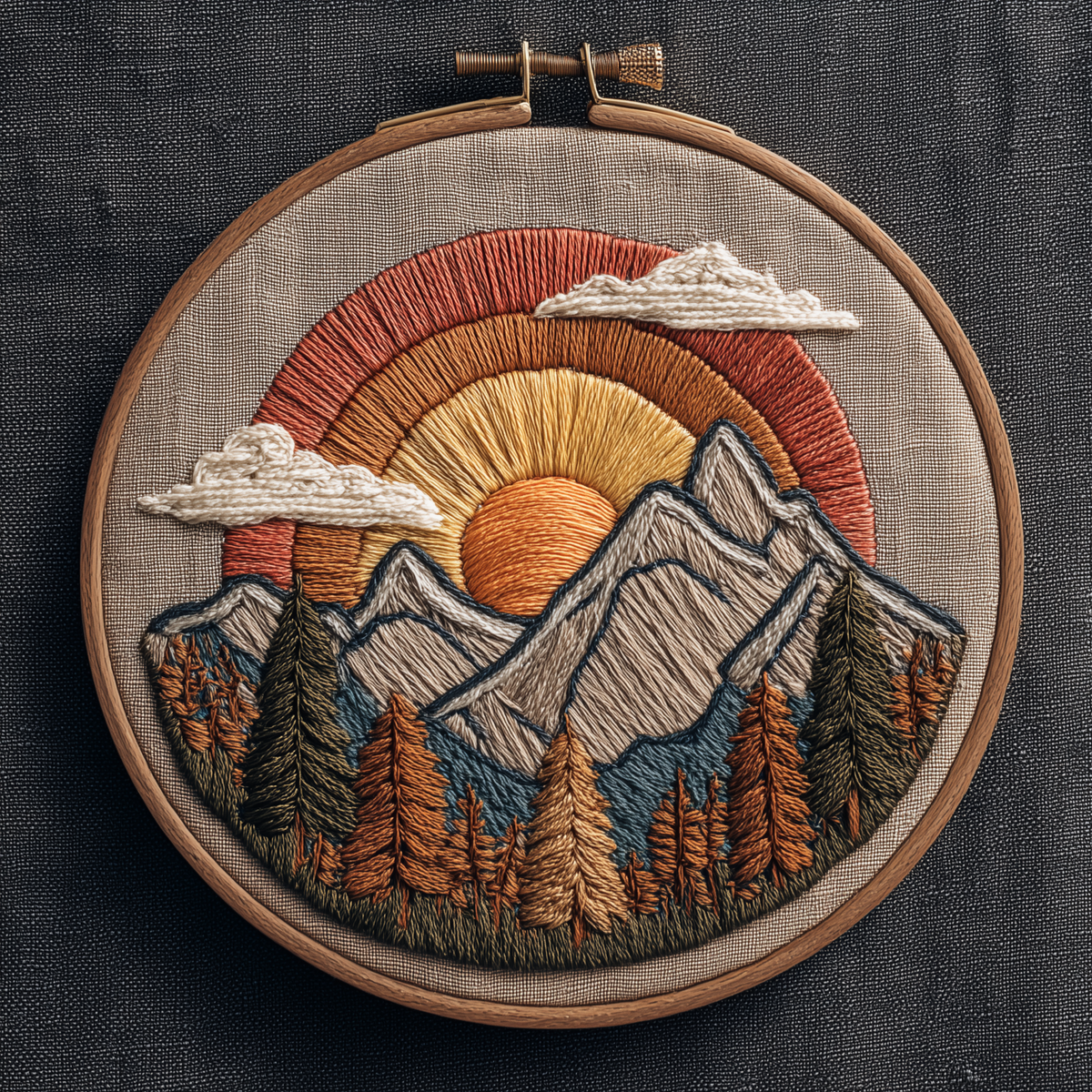 Layered sun setting behind grey peaks and an autumn pine forest in a wooden embroidery hoop, photographed in full on dark linen